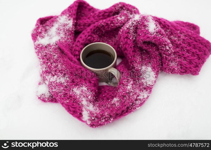 season, drinks, christmas and winter holidays concept - tea or coffee mug and knitted woolen scarf on snow