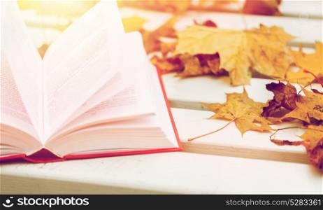 season, education and literature concept - open book and autumn leaves on park bench. open book and autumn leaves on park bench