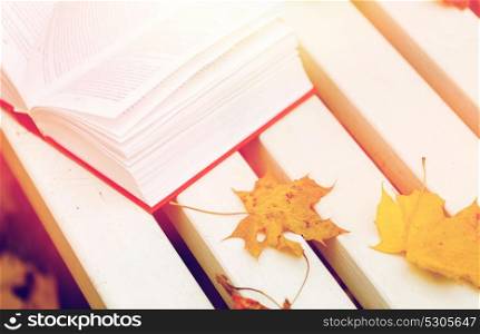 season, education and literature concept - open book and autumn leaves on park bench. open book and autumn leaves on park bench