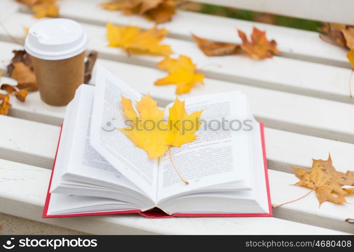 season, education and literature concept - open book and coffee cup on bench in autumn park