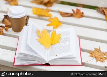 season, education and literature concept - open book and coffee cup on bench in autumn park