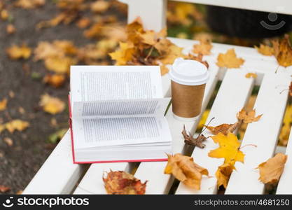 season, education and literature concept - open book and coffee cup on bench in autumn park