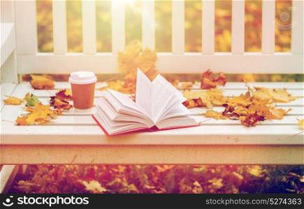 season, education and literature concept - open book and coffee cup on bench in autumn park. open book and coffee cup on bench in autumn park