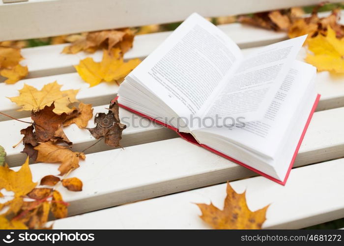 season, education and literature concept - open book on bench in autumn park