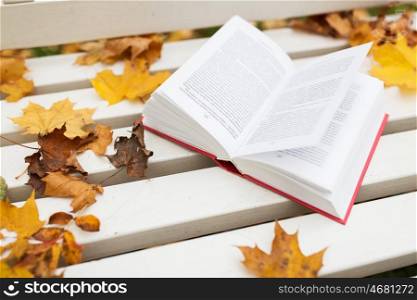 season, education and literature concept - open book on bench in autumn park