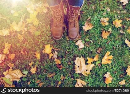 season, footwear and people concept - female feet in boots with autumn leaves on grass. female feet in boots and autumn leaves on grass