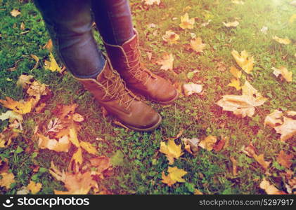 season, footwear and people concept - female feet in boots with autumn leaves on grass. female feet in boots and autumn leaves on grass