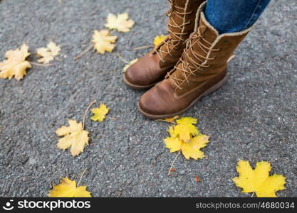 season, footwear and people concept - female feet in boots with autumn leaves on ground