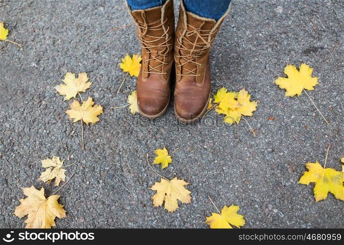 season, footwear and people concept - female feet in boots with autumn leaves on ground