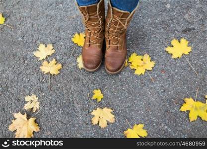 season, footwear and people concept - female feet in boots with autumn leaves on ground