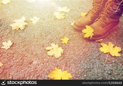 season, footwear and people concept - female feet in boots with autumn leaves on ground. female feet in boots and autumn leaves
