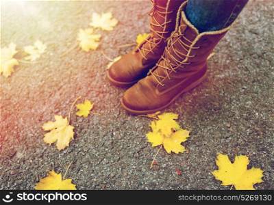 season, footwear and people concept - female feet in boots with autumn leaves on ground. female feet in boots and autumn leaves