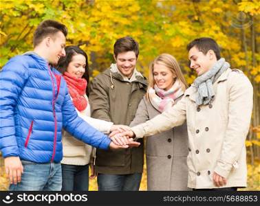season, friendship, gesture and people concept - group of smiling men and women with hands on top in autumn park