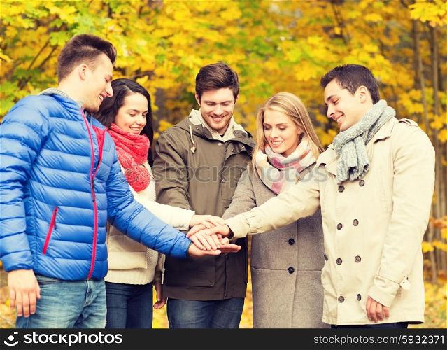 season, friendship, gesture and people concept - group of smiling men and women with hands on top in autumn park