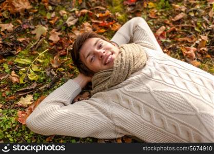 season, happiness and people concept - close up of smiling young man lying on ground or grass and fallen leaves in autumn park