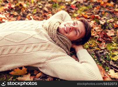 season, happiness and people concept - close up of smiling young man lying on ground or grass and fallen leaves in autumn park