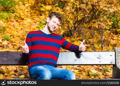 Season, happiness and people concept. Young bearded man sitting relaxed on bench in autumnal park on sunny day . man sitting on the bench in park