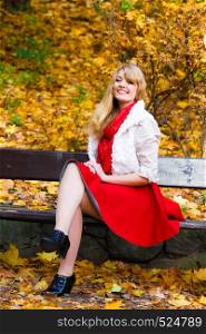 Season, happiness and people concept. Young fashionable blonde woman in full lehgth sitting on bench in autumnal park on sunny day . Woman sitting on bench in park