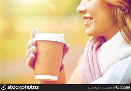 season, hot drinks, advertisement and people concept - close up of beautiful happy young woman drinking coffee or tea from disposable paper cup in autumn park. close up of happy woman with coffee in autumn park