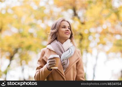 season, hot drinks and people concept - beautiful happy young woman drinking coffee or tea from disposable paper cup in autumn park