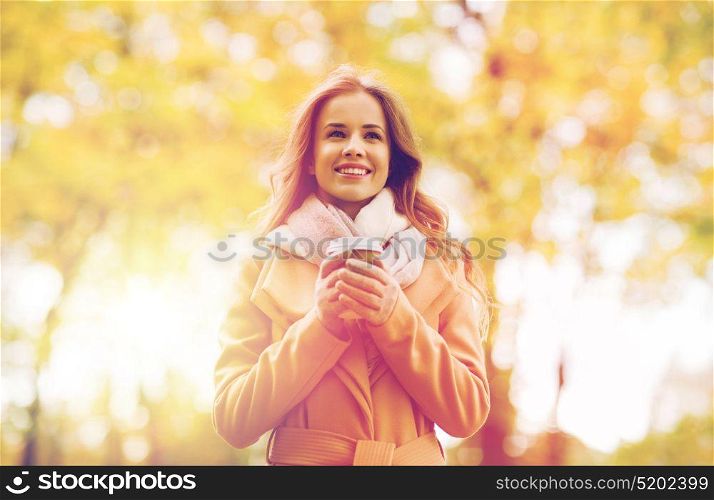 season, hot drinks and people concept - beautiful happy young woman drinking coffee or tea from disposable paper cup in autumn park. happy young woman drinking coffee in autumn park