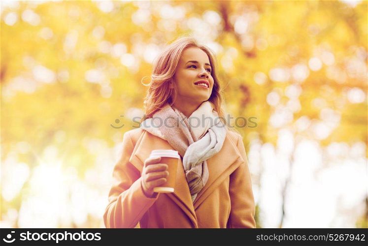 season, hot drinks and people concept - beautiful happy young woman drinking coffee or tea from disposable paper cup in autumn park. happy young woman drinking coffee in autumn park