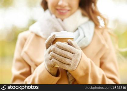 season, hot drinks and people concept - close up of beautiful happy young woman drinking coffee or tea from disposable paper cup in autumn park