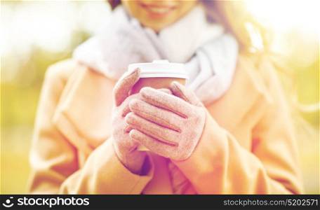 season, hot drinks and people concept - close up of beautiful happy young woman drinking coffee or tea from disposable paper cup in autumn park. close up of happy woman with coffee in autumn park