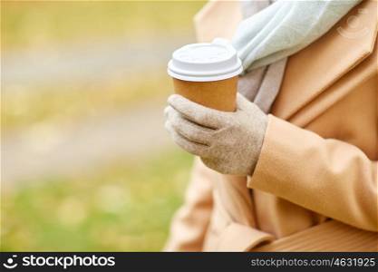 season, hot drinks and people concept - close up of woman with coffee or tea disposable paper cup in autumn park