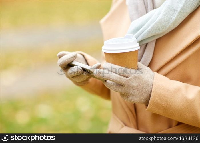 season, hot drinks and people concept - close up of woman with smartphone and disposable coffee or tea paper cup in autumn park