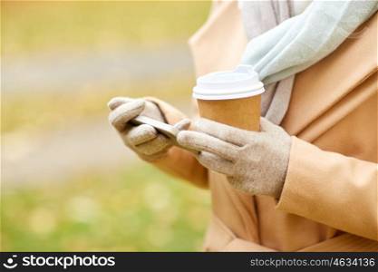 season, hot drinks and people concept - close up of woman with smartphone and disposable coffee or tea paper cup in autumn park