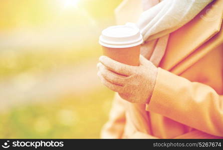 season, hot drinks and people concept - close up of woman with coffee or tea disposable paper cup in autumn park. close up of woman with coffee in autumn park