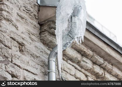 season, housing and winter concept - icicles hanging from building drainpipe