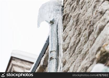 season, housing and winter concept - icicles hanging from building drainpipe