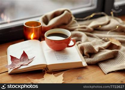 season, leisure and objects concept - cup of coffee, book, autumn leaves and candle on window sill at home. cup of coffee, book on window sill in autumn
