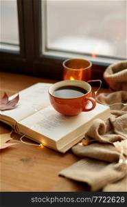 season, leisure and objects concept - cup of coffee, book, autumn leaves and candle on window sill at home. cup of coffee, book on window sill in autumn