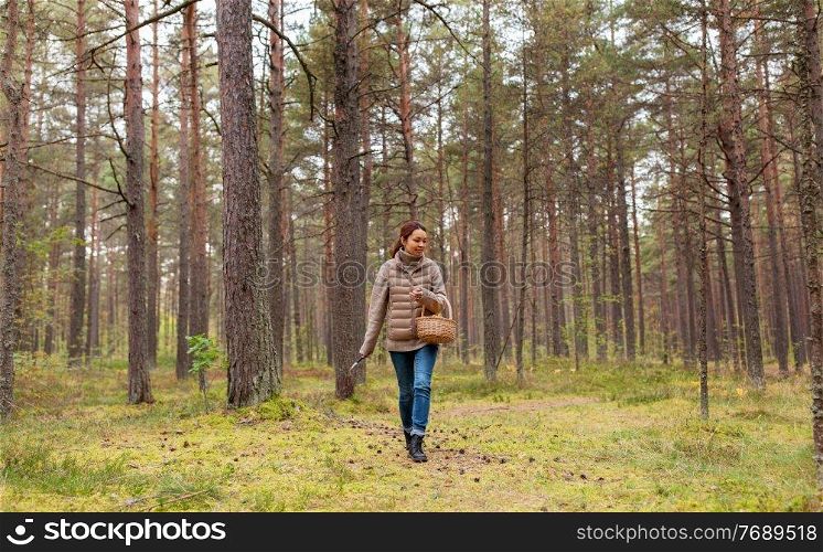 season, leisure and people concept - young asian woman with basket walking in autumn forest and picking mushrooms. young woman picking mushrooms in autumn forest
