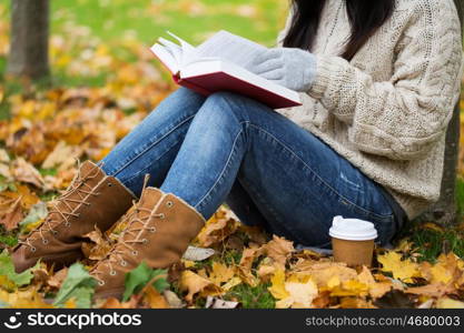 season, literature, education and people concept - close up of young woman reading book and drinking coffee from paper cup in autumn park