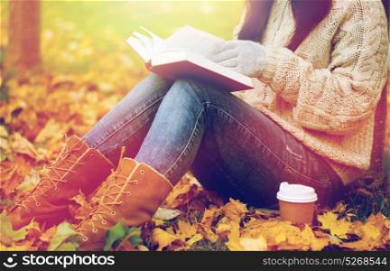 season, literature, education and people concept - close up of young woman reading book and drinking coffee from paper cup in autumn park. woman with book drinking coffee in autumn park