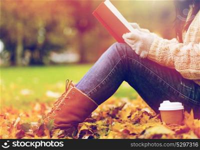season, literature, education and people concept - close up of young woman reading book and drinking coffee from paper cup in autumn park. woman with book drinking coffee in autumn park