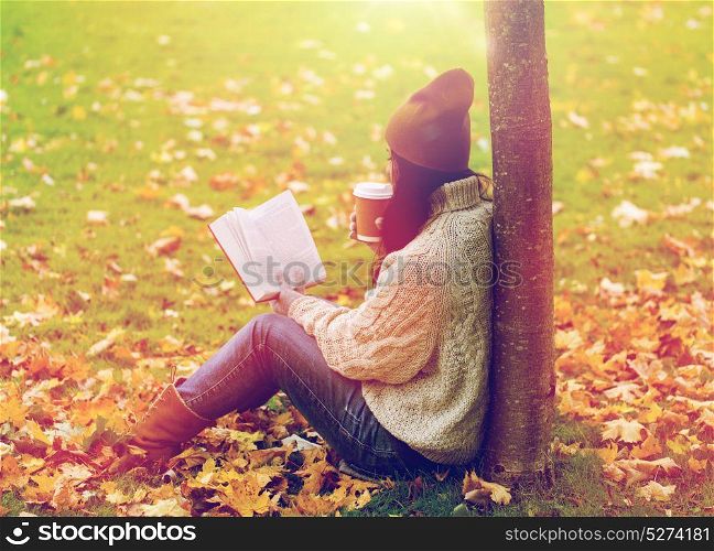 season, literature, education and people concept - young woman reading book and drinking coffee from paper cup in autumn park. woman with book drinking coffee in autumn park