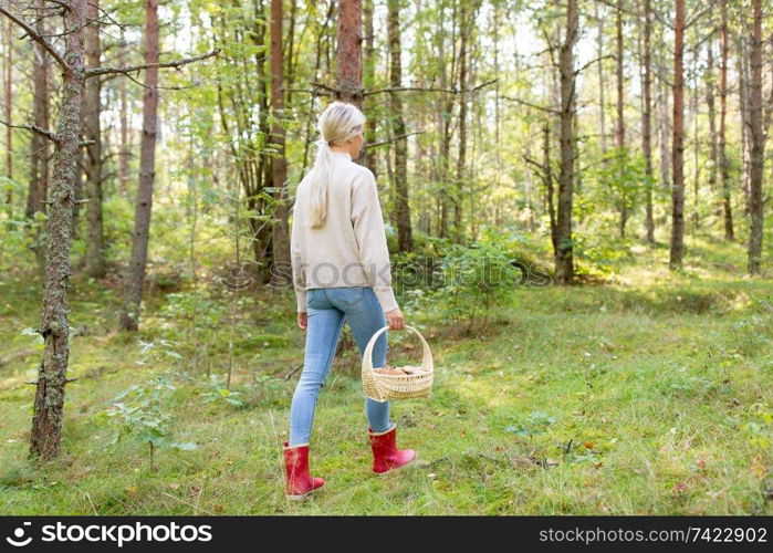 season, nature and leisure concept - young woman with mushrooms in basket walking along autumn forest. young woman picking mushrooms in autumn forest