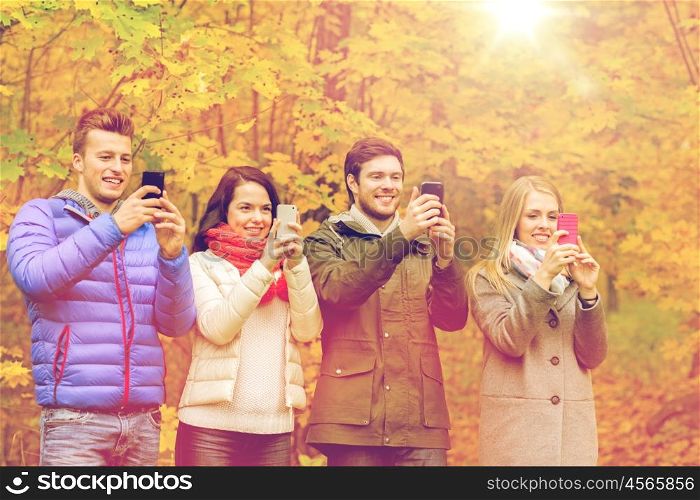 season, people, technology and friendship concept - group of smiling friends with smartphones taking picture or playing augmented reality game in autumn park