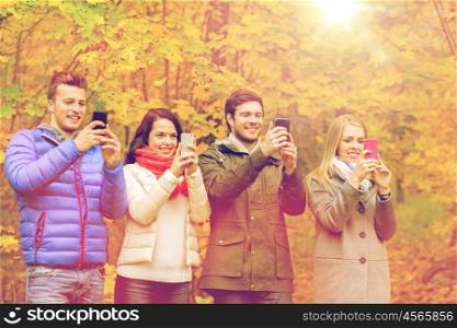 season, people, technology and friendship concept - group of smiling friends with smartphones taking picture or playing augmented reality game in autumn park