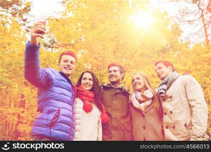 season, people, technology and friendship concept - group of smiling friends with smartphone taking selfie in autumn park