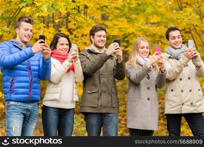 season, people, technology and friendship concept - group of smiling friends with smartphones taking picture in autumn park