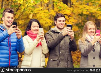 season, people, technology and friendship concept - group of smiling friends with smartphones taking picture in autumn park