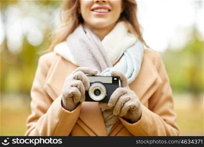 season, photography and people concept - close up of happy smiling young woman taking picture with vintage camera in autumn park