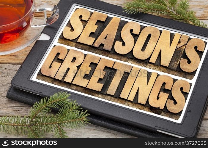 season&rsquo;s greetings typography - text in letterpress wood type on a digital tablet with a cup of tea