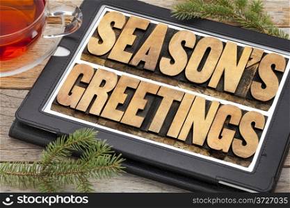 season&rsquo;s greetings typography - text in letterpress wood type on a digital tablet with a cup of tea